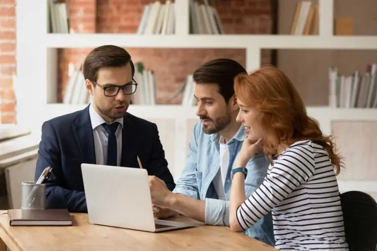 Three people discussing a Lux Custom Home Consultation at a table, focused on a laptop.